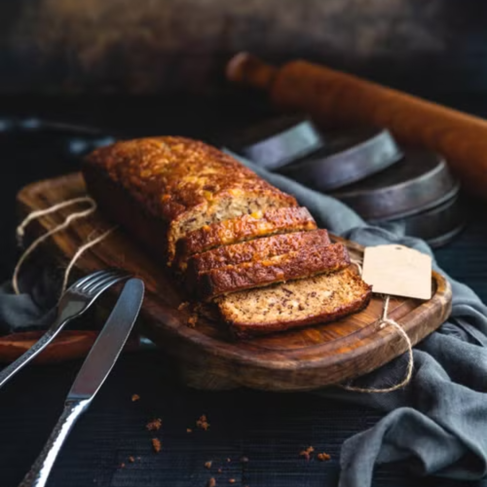 Banana bread batter made with Greek yogurt being poured into a loaf pan, with ripe bananas and baking ingredients arranged neatly on a modern kitchen counter.